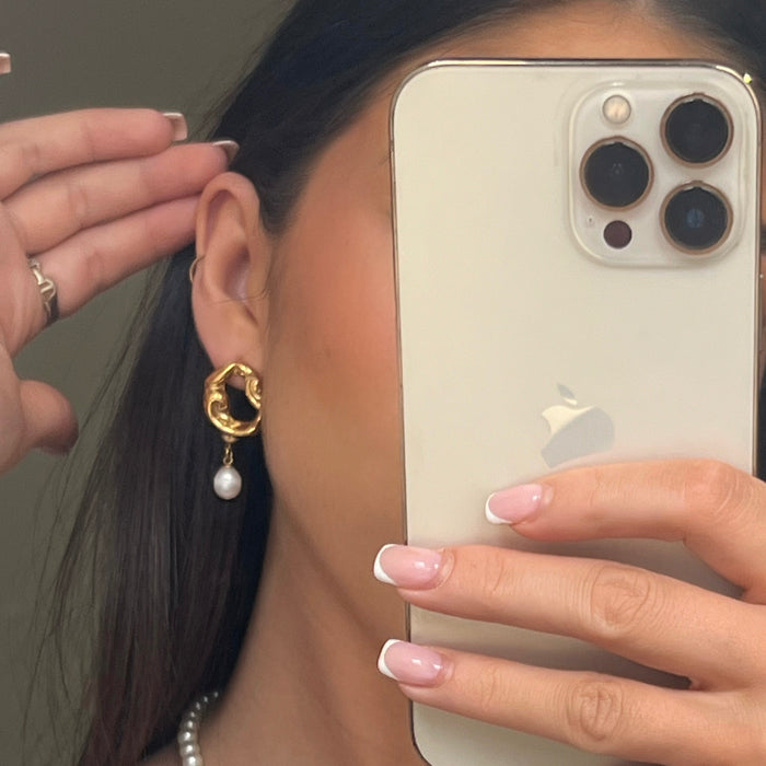 model wearing Gold earrings with pearl drops, abstract design.