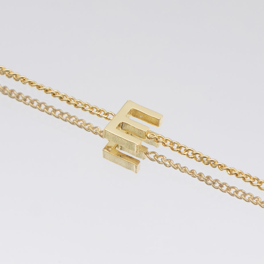 Maia mini initial bracelet in 18k gold featuring a delicate link chain and an elegant 'E' pendant.