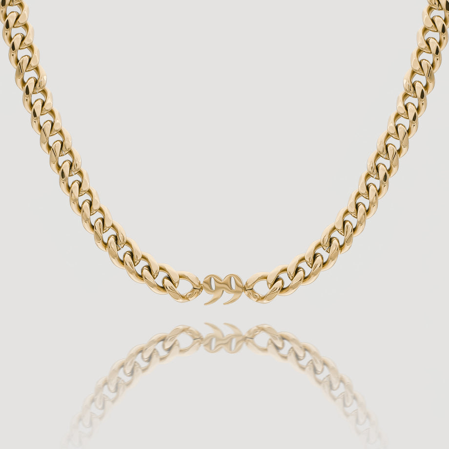 Gold chain necklace on a reflective surface.
