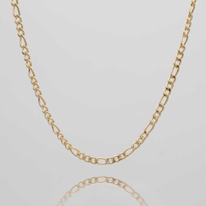 Gold Figaro chain on reflective surface.