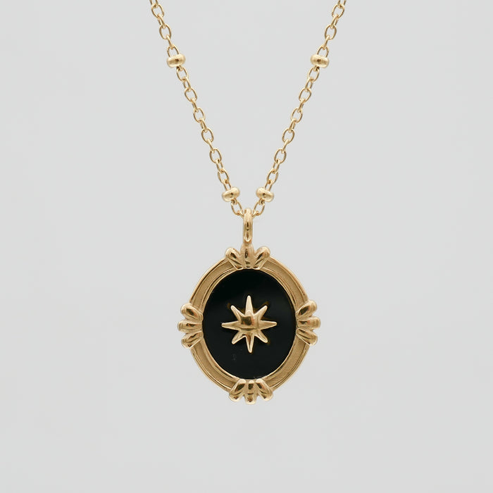 Gold necklace with black pendant and star design.
