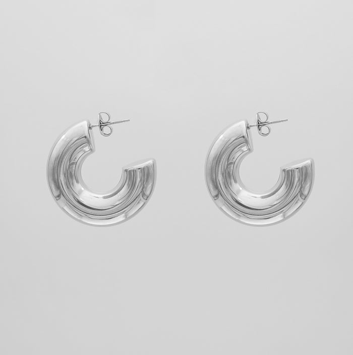 silver chunky half hoop earrings against a grey background.