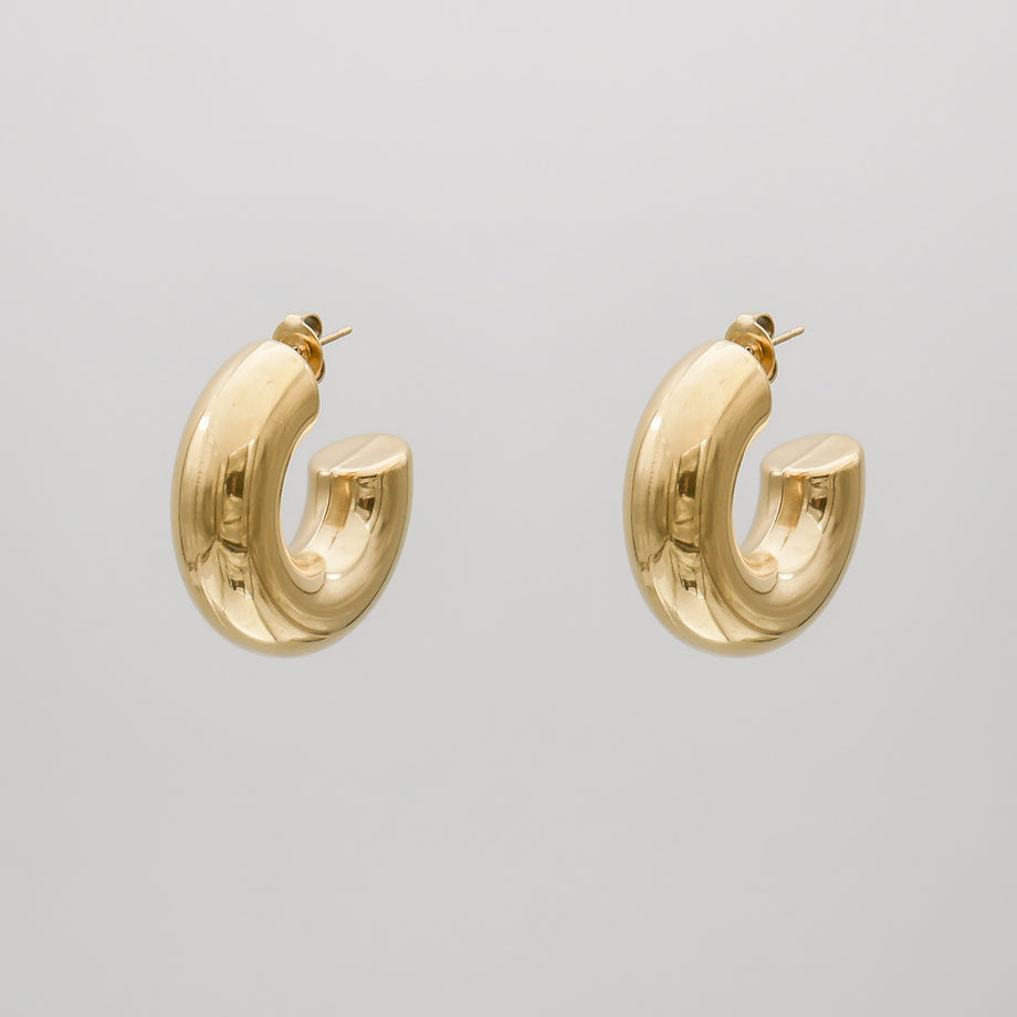 gold chunky half hoop earrings against a grey background.