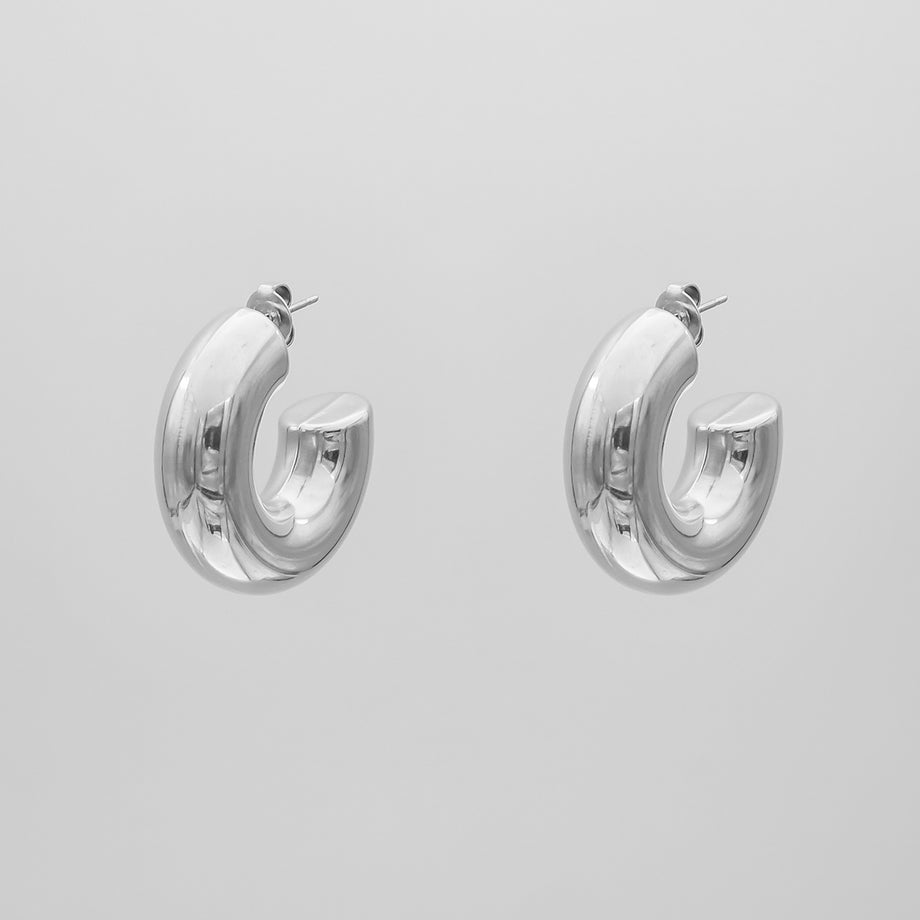 silver chunky half hoop earrings against a grey background.