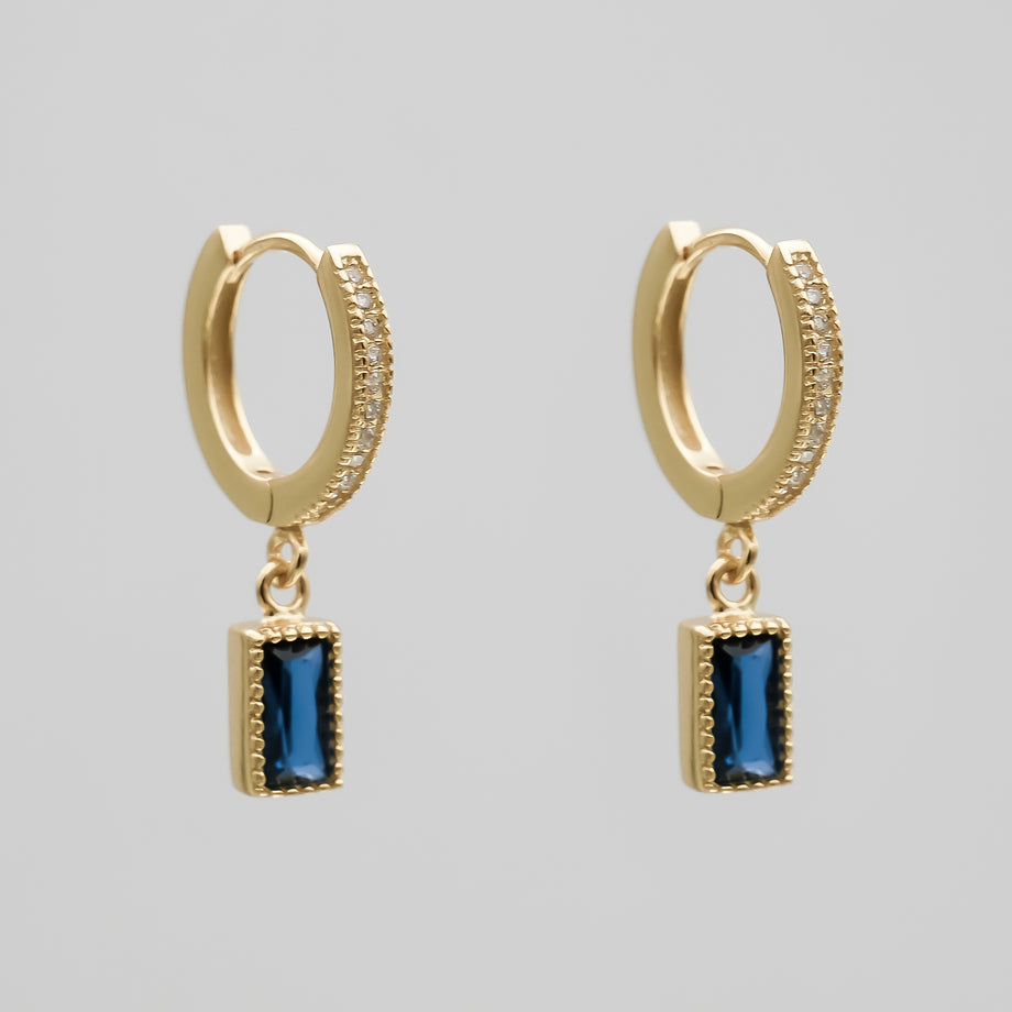 Gold pave hoop earrings with blue gemstone pendants.