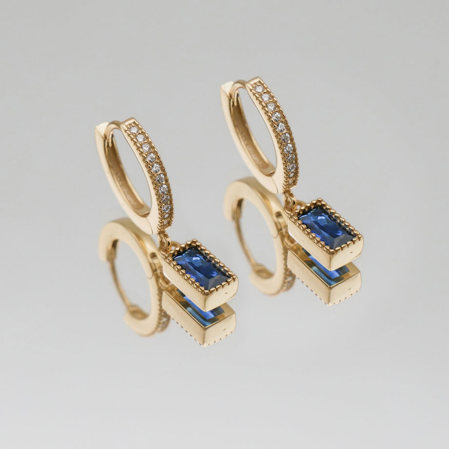 Gold pave hoop earrings with blue gemstone pendants.