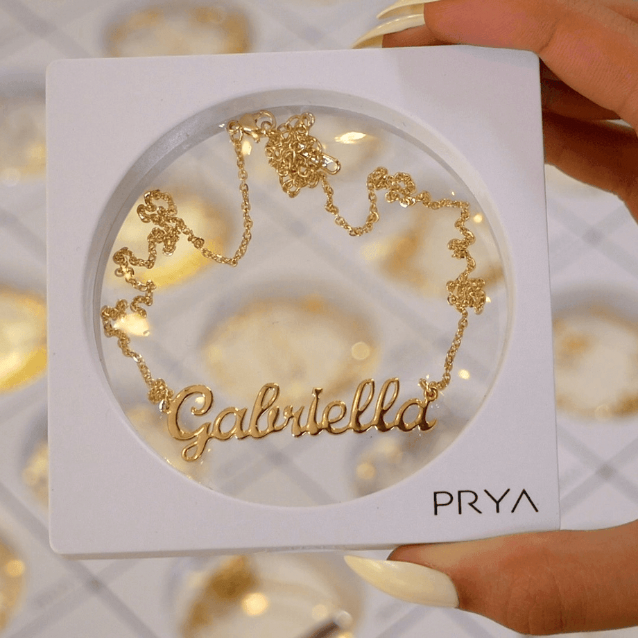 Gold custom name necklace in display box held above lots of custom name necklaces in background