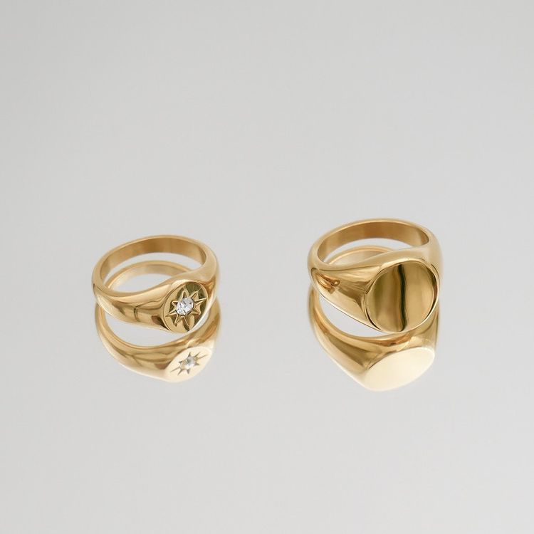 Can Women Wear Signet Rings? Two gold signet rings on a white background. One ring has a plain, solid gold facing while the other features a cubic zirconia gem in the center