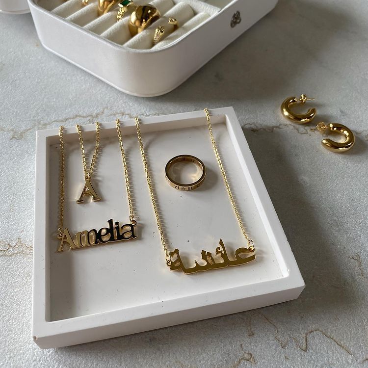 Personalised Jewellery in a gift box, including a name necklace, arabic name necklace, and a ring. To the side are small gold hoop rings and a jewellery storage box.