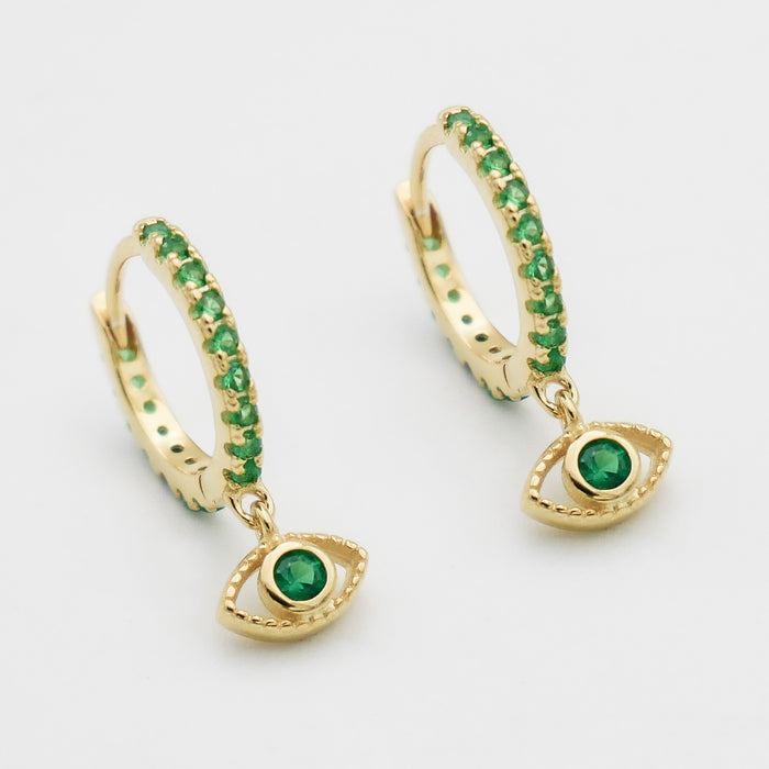 close up of gold evil eye huggie earring paved with emerald