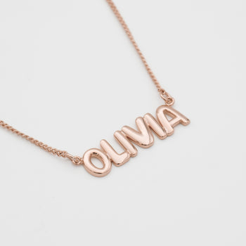 model wearing Bubble custom name necklace, with gold, silver and rose gold option, featuring ballon-shaped letters, charms, and the & symbol on multiple chain options