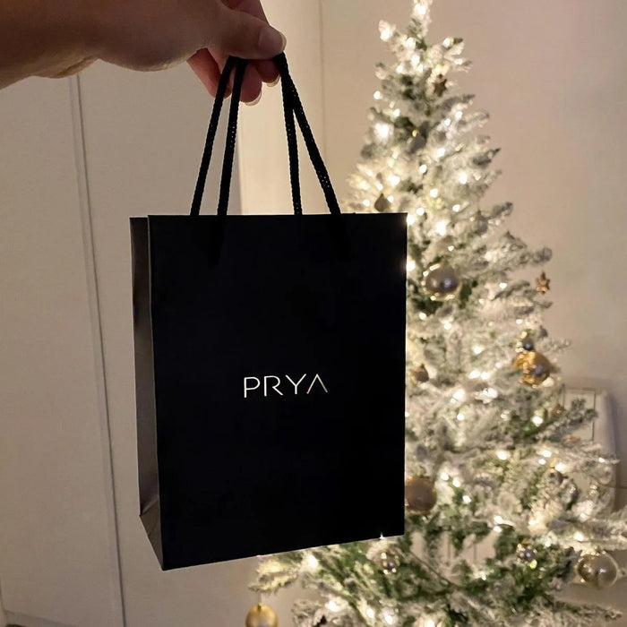 Hand holding a PRYA gift bag near Christmas tree.