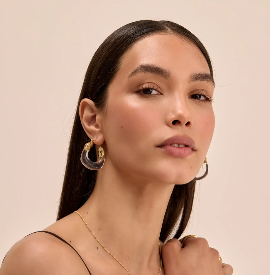 model wearing clear celine earrings in gold and chunky gold rings from prya