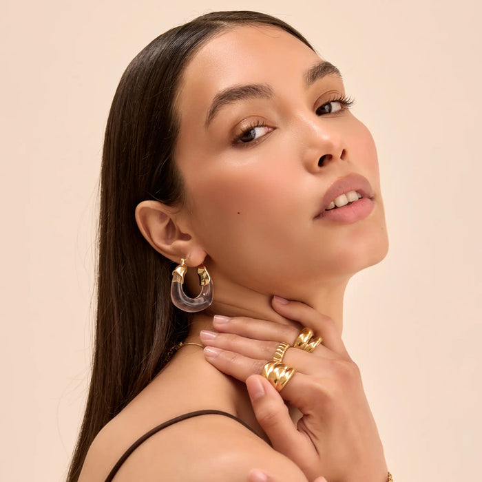model wearing clear celine earrings in gold and chunky gold rings from prya