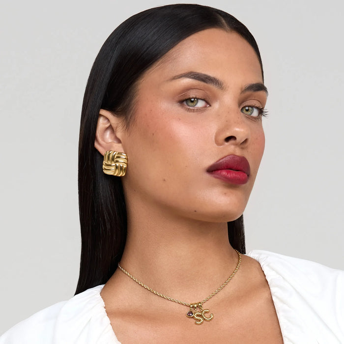 Woman wearing gold earrings and necklace against a neutral background
