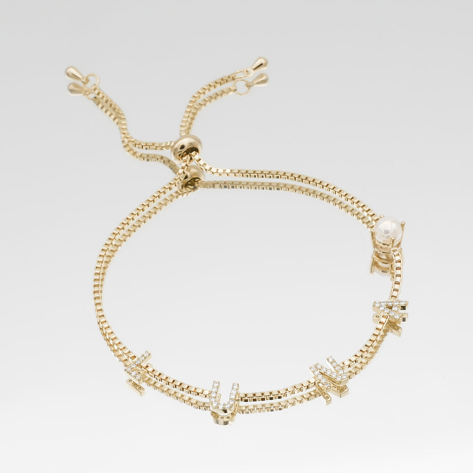 Gold bracelet with diamond-encrusted letters and pearl.