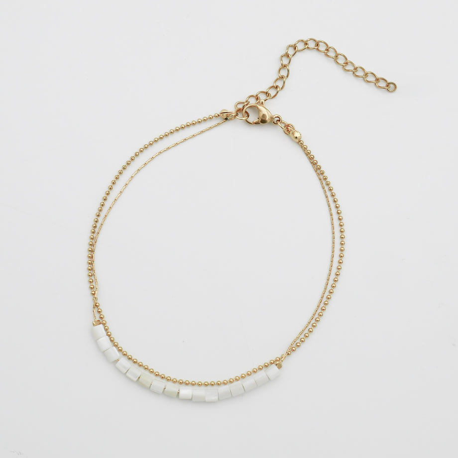 Gold anklet with white beads on white background.