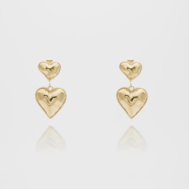 Gold heart-shaped dangling earrings on white background.