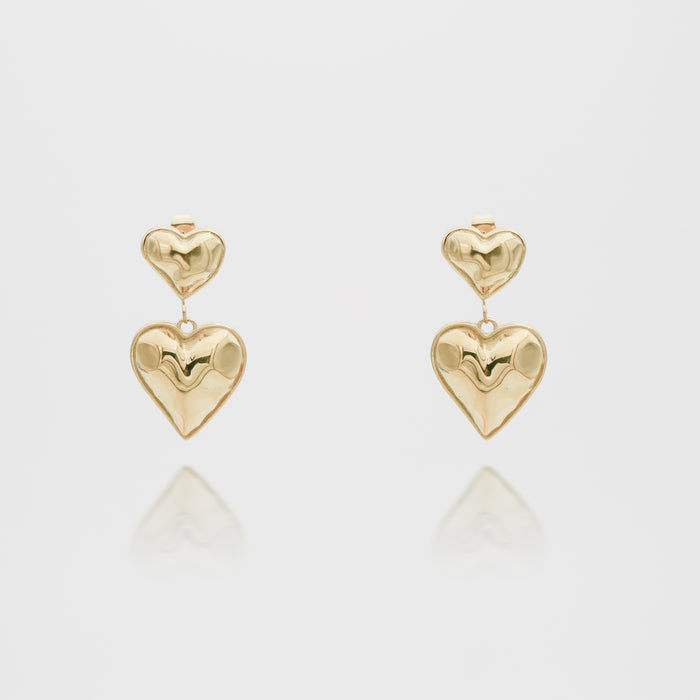 Gold heart-shaped dangling earrings on white background.