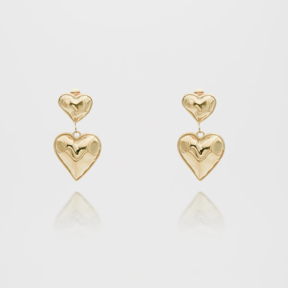 Gold heart-shaped dangling earrings on white background.