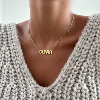 model wearing Bubble custom name necklace, with gold, silver and rose gold option, featuring ballon-shaped letters, charms, and the & symbol on multiple chain options