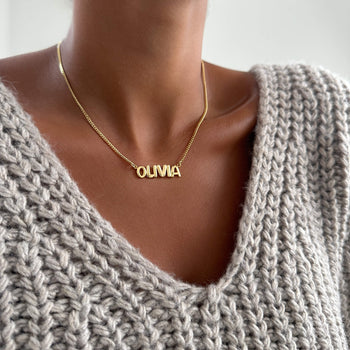 model wearing model wearing Bubble custom name necklace, with gold, silver and rose gold option, featuring ballon-shaped letters, charms, and the & symbol on multiple chain options