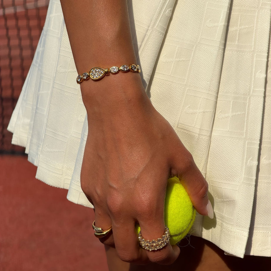 model wearing luxury padel bracelet in 18k gold vermeil. Oval stones and pavé padel racket charm.