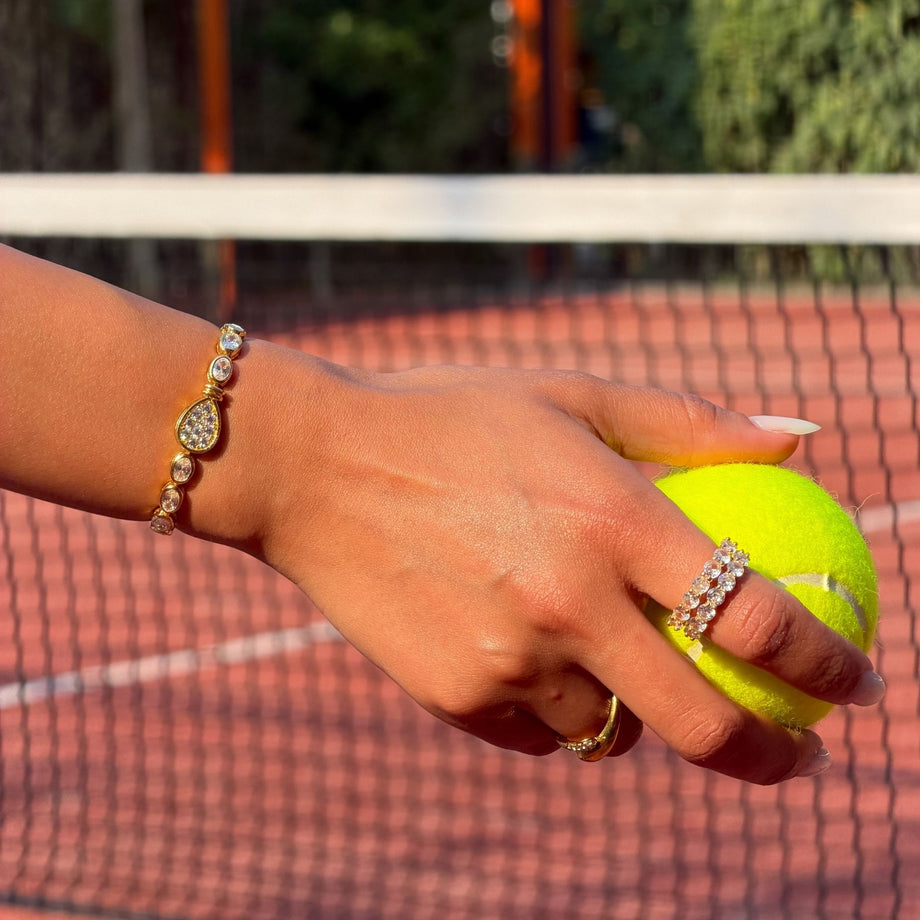model wearing bold, luxury padel bracelet in 18k gold vermeil. Oval stones and pavé padel racket charm.