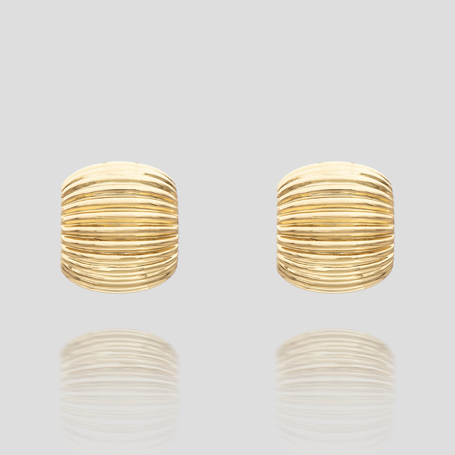 Gold ribbed stud earrings on grey background.