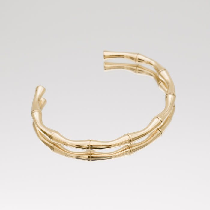 Gold bamboo-style open bracelet on white background.