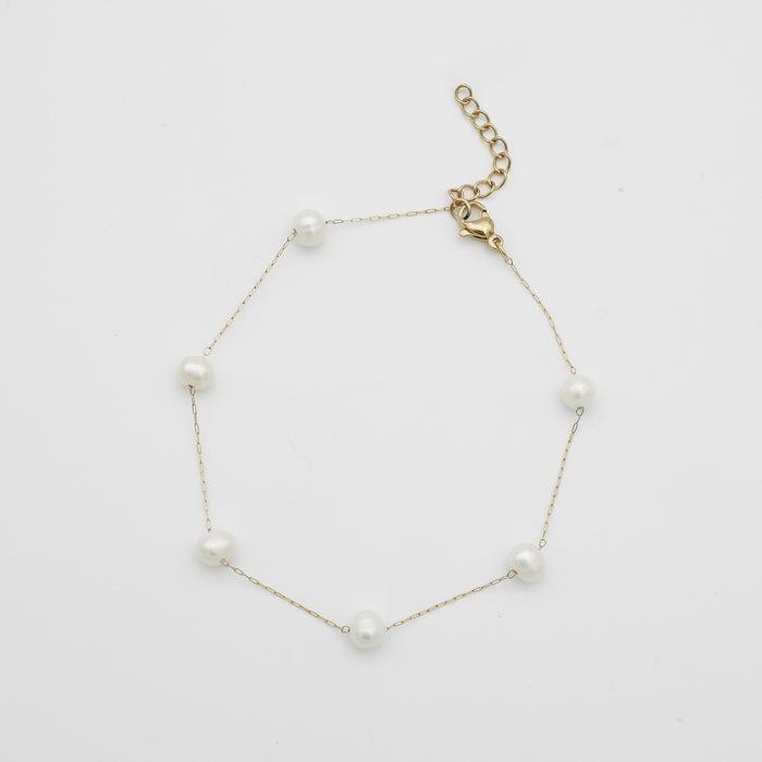 Gold anklet with pearls on white background.