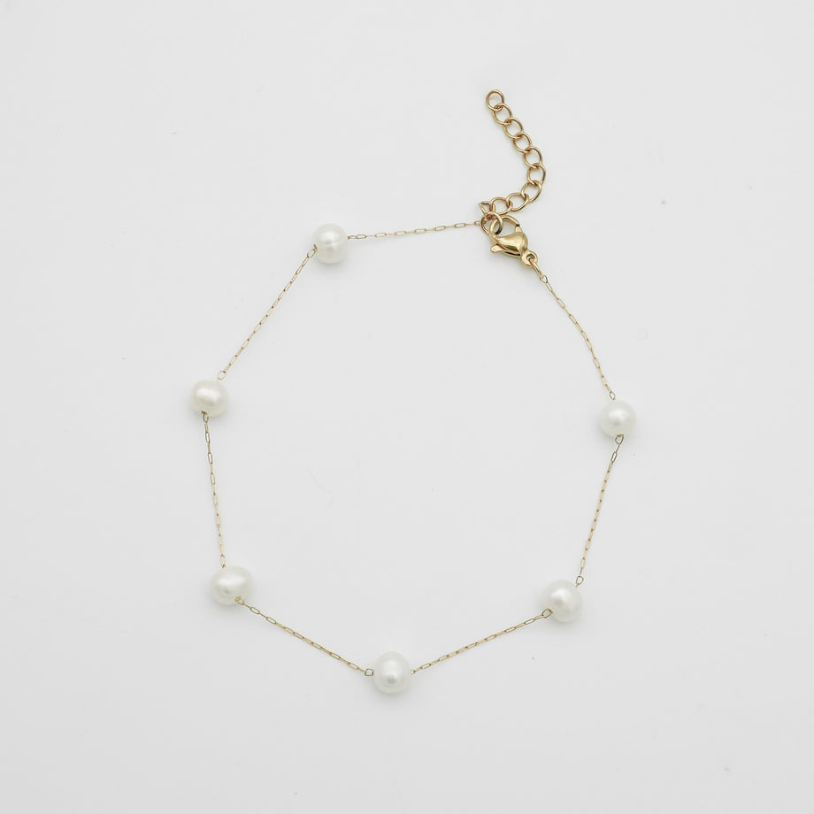 Gold anklet with pearls on white background.