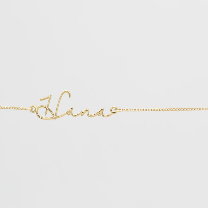 Gold script name necklace on white background.