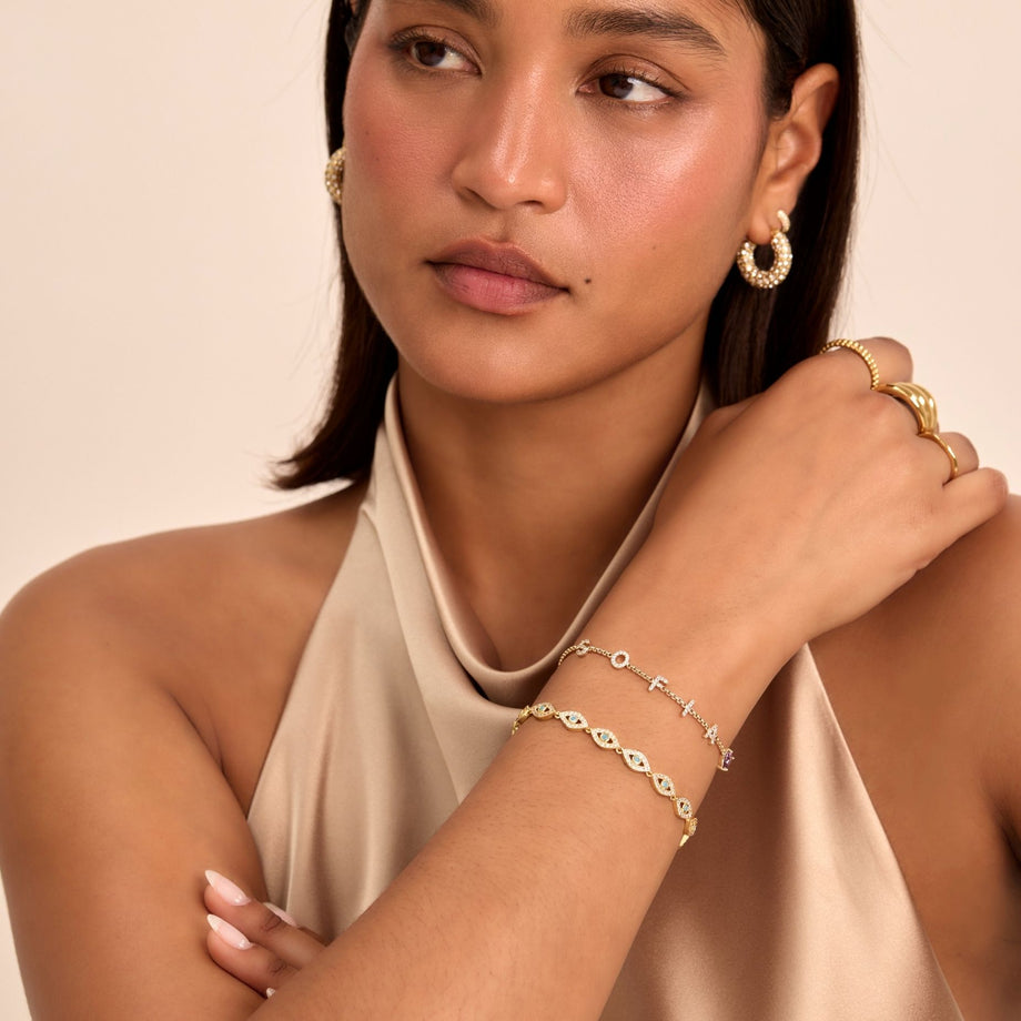 model wearing stacked bracelets, evil eye bracelet and custom name bracelet in gold from prya