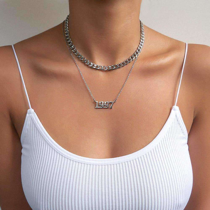  Woman in white strappy top wearing 1997 silver birth year necklace and Cuban link Chain necklace.