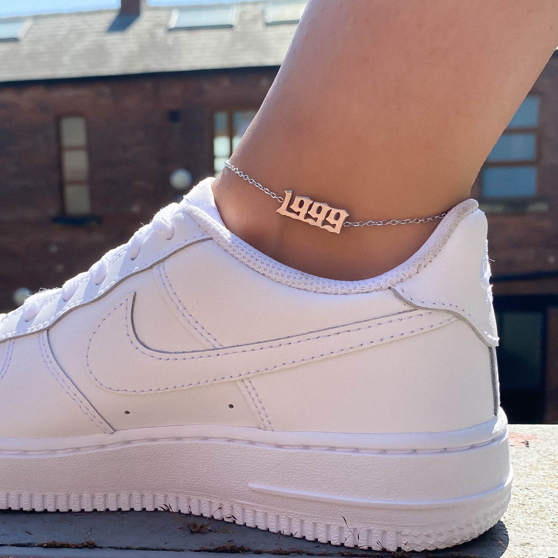 A sunny shot of a silver birth year anklet while wearing white nike sneakers.