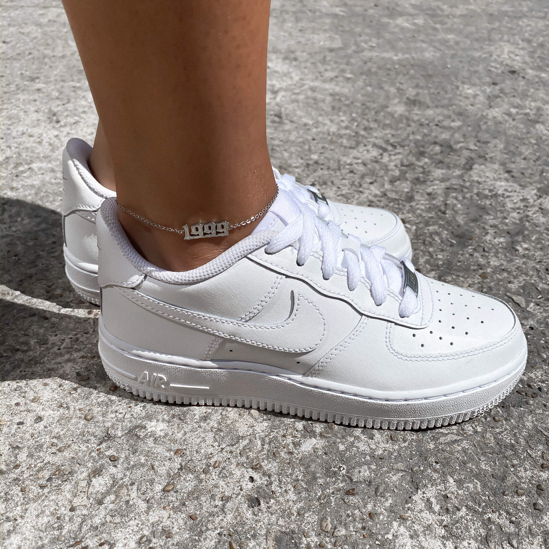 A woman wearing a 1999 silver birth year anklet and white sneakers