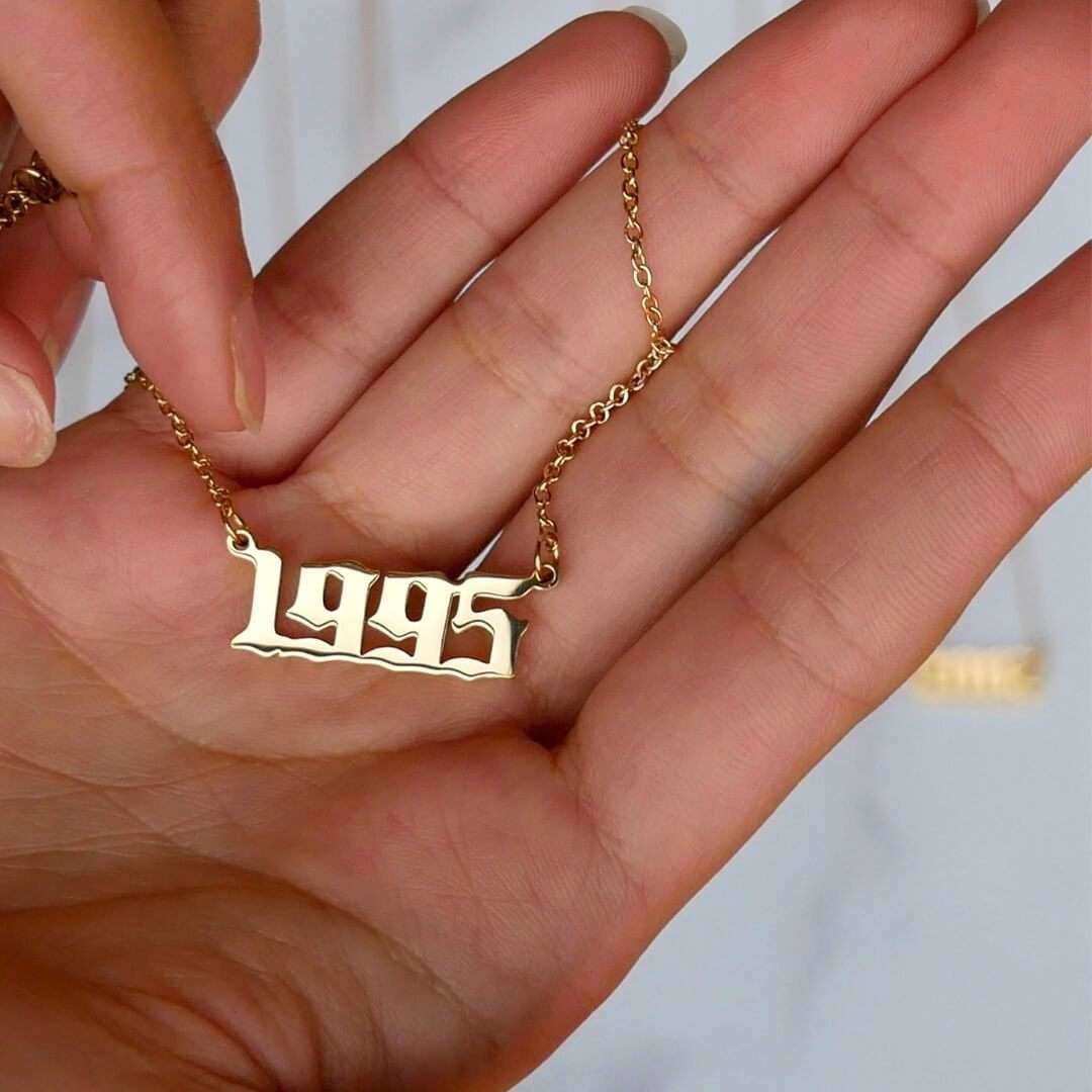 Hand holding a gold birth year necklace with a 1995 pendant