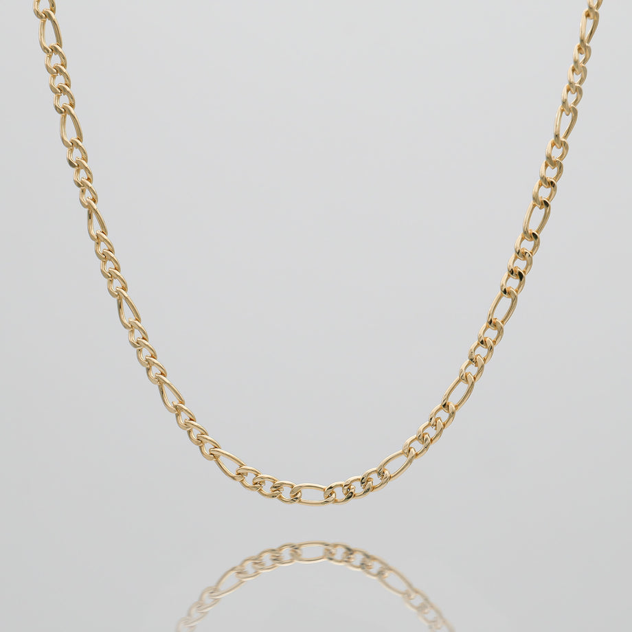 Gold Figaro chain on reflective surface.