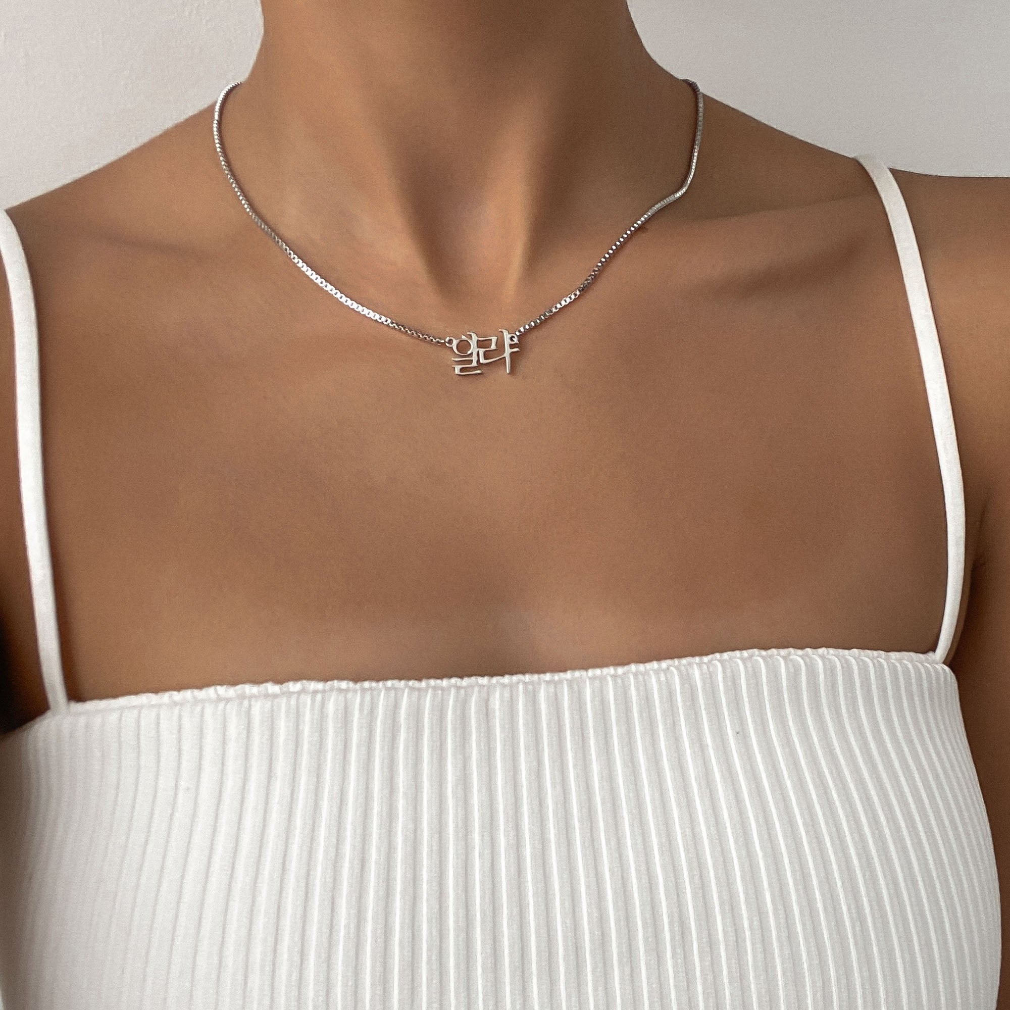 Woman wearing a white strappy top and sporting a silver Korean name necklace