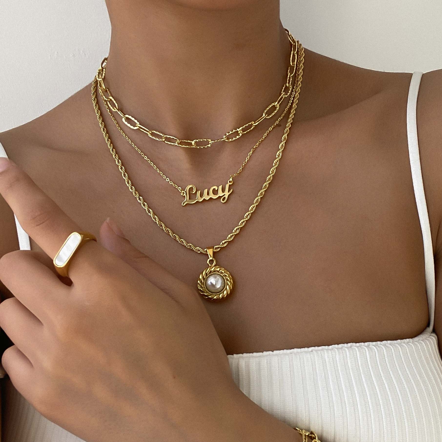 Woman wearing custom name necklace, gold pendant necklace and paperclip chain as well as a woman’s signet ring