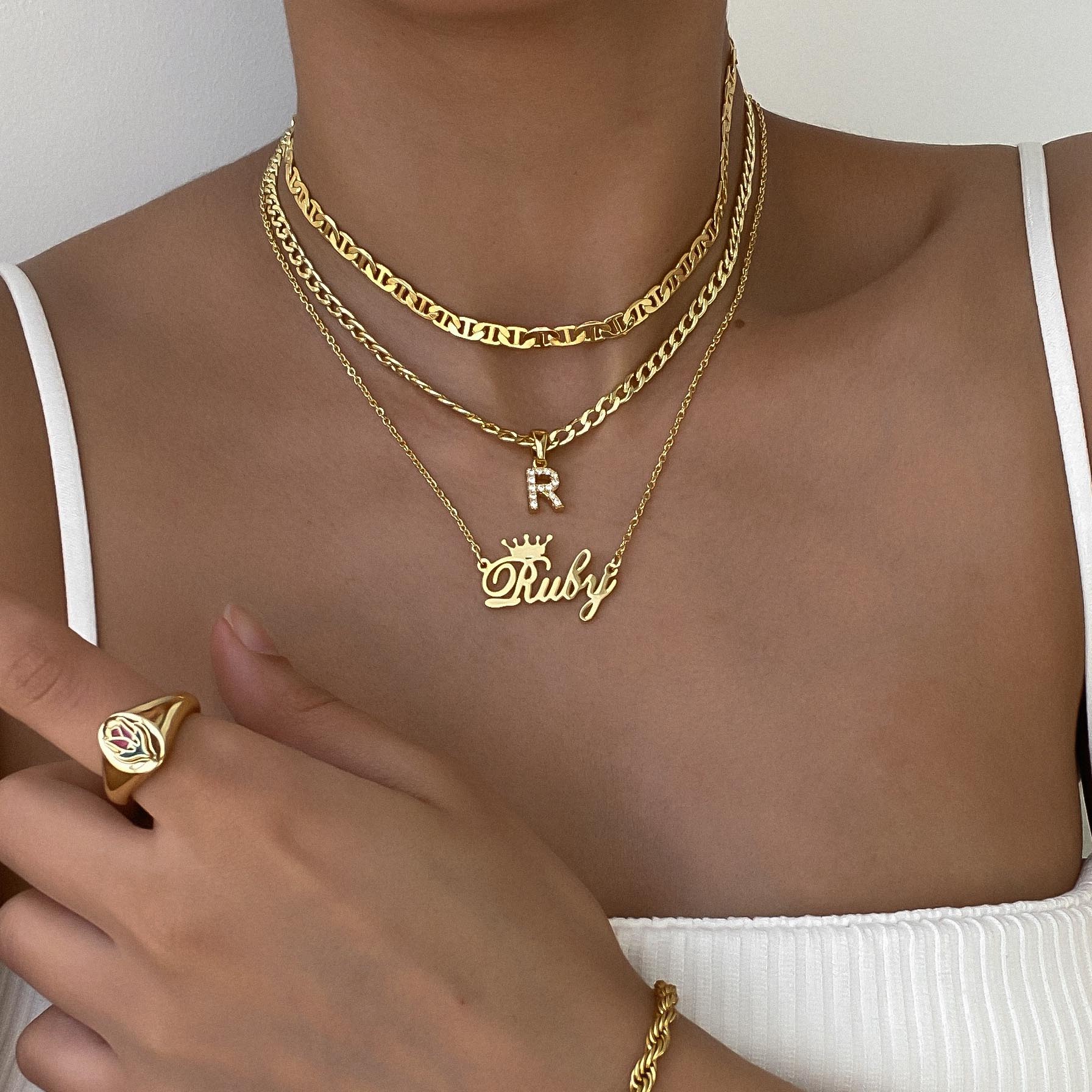 A woman wearing a gold customised necklace, initial necklace and gold chain, and a signet ring and bracelet chain.