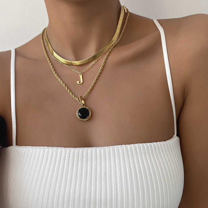 Layered gold necklaces featuring an initial pendant and a black charm, showcasing a chic and stylish look.