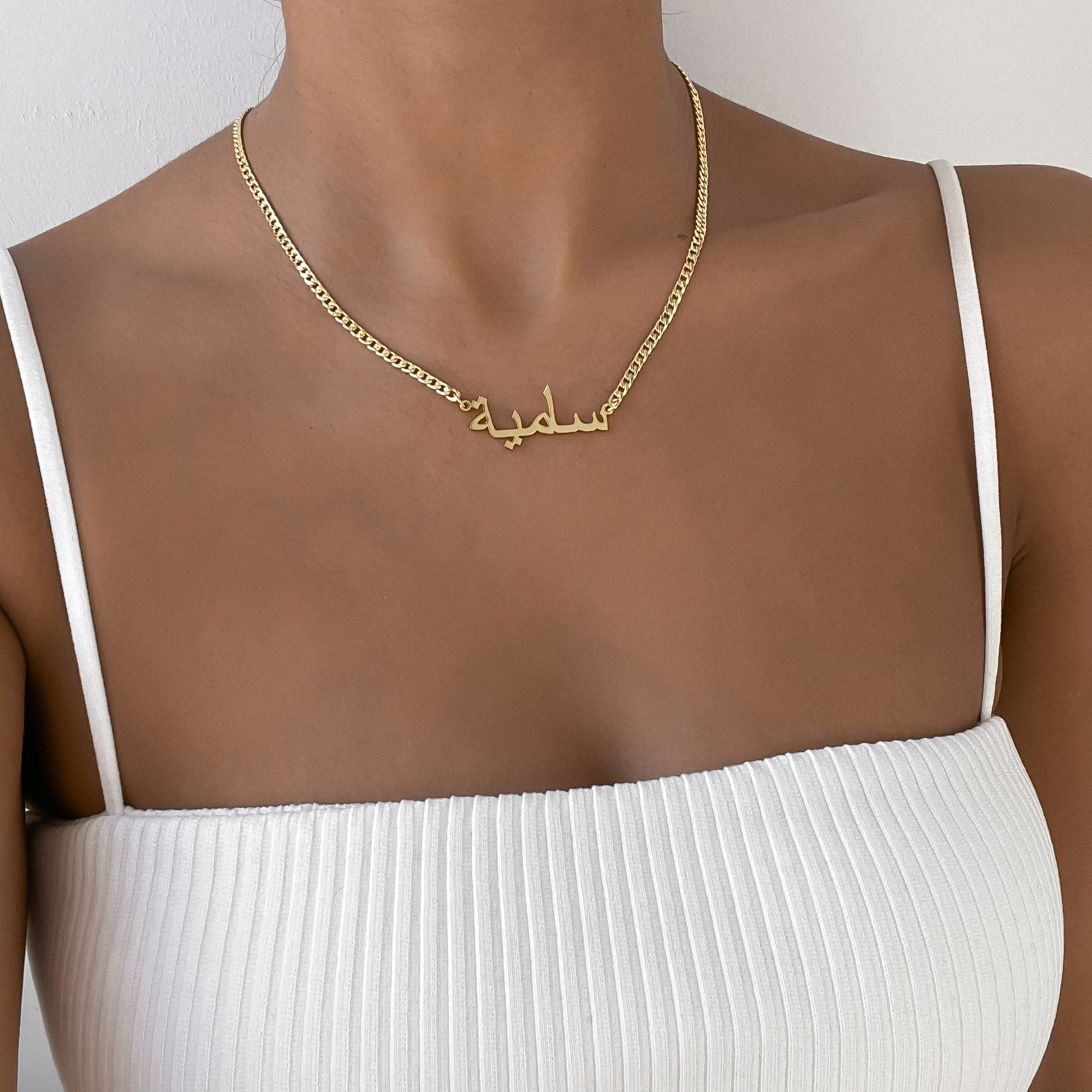 A woman wearing a white strappy top and an Arabic name necklace