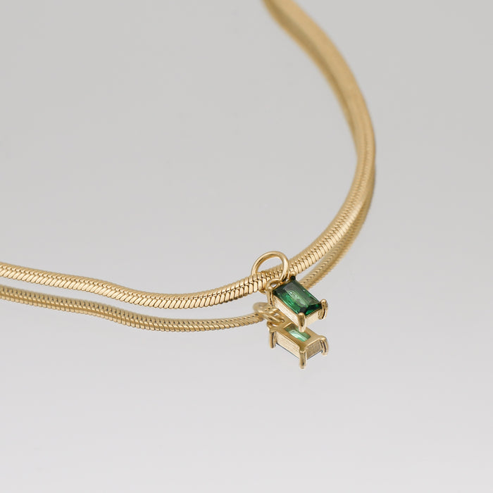 Gold necklace with emerald pendant on display.