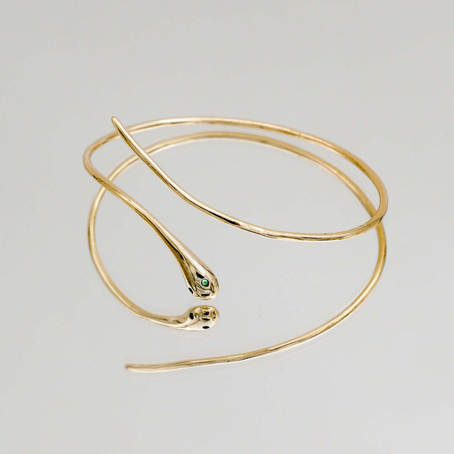 Gold snake-shaped bracelet on a reflective surface.