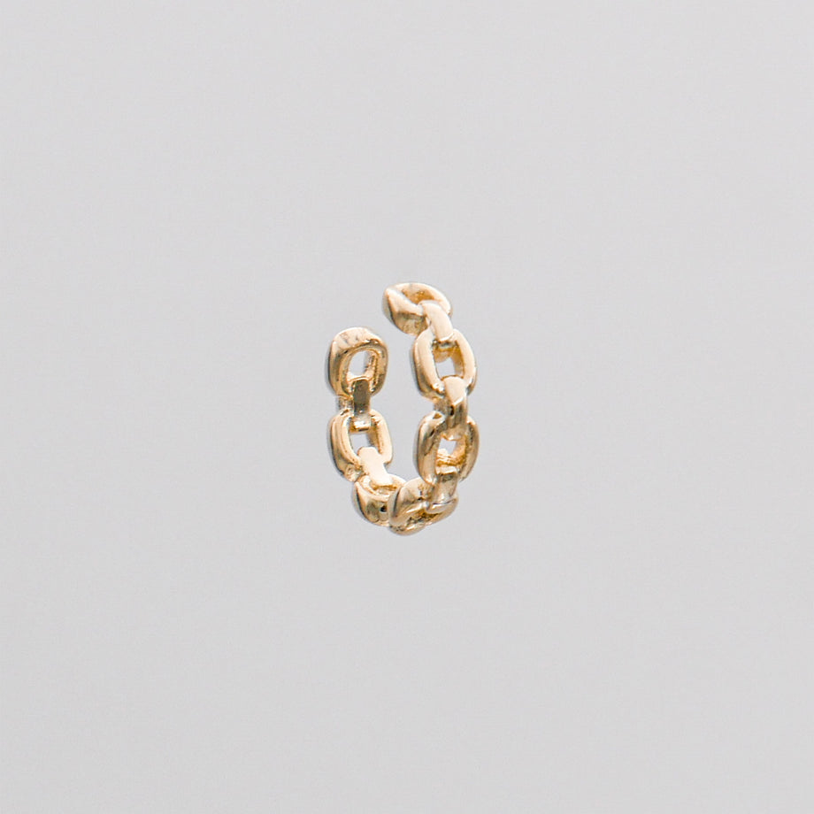 Gold chain link ear cuff on grey background.