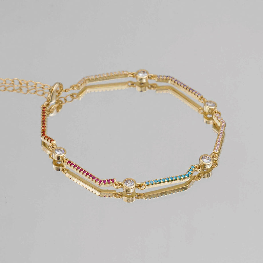 Gold bracelet with colourful gemstones on grey background.