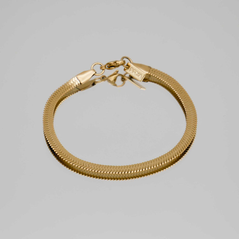 Gold snake chain bracelet on grey background.