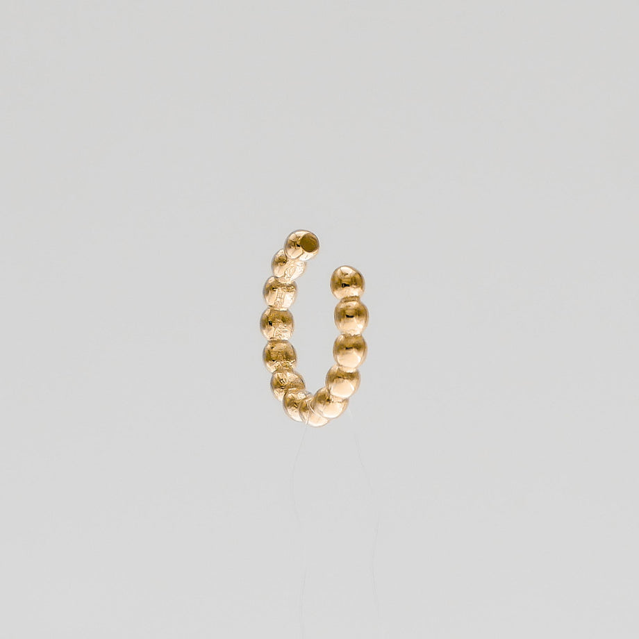 Gold beaded open ring against grey background.